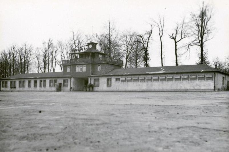 Blick über den leeren Appellplatz auf das Torgebäude. Am rechten Anbau sind die Fensterverblendungen des Arrestzellenbaus zu erkennen.